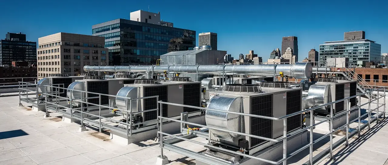 Row of rooftop units and ductwork on a commercial roof with the city behind